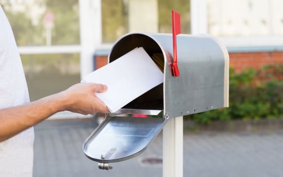 Close-up Of Person Putting Stack Of Letters In Mailbox
