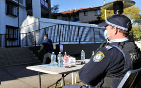 A police officer stays guard outside an isolated residential building in Sydney's western suburb of Blacktown after several cases were reported among the residents.