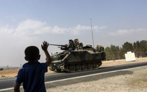 A Turkish boy waves to a Turkish tank driving into Syria from the Turkish Syrian border city of Karkamis in the southern region of Gaziantep, on August 26, 2016.