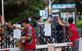 Delivery workers pass packages over a fence to residents in Xicheng District of Beijing. 17 June 2020, after a new Covid-19 outbreak.
