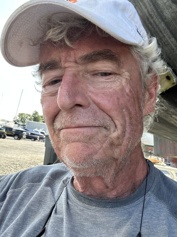 John smiles slightly and is wearing a white cap.