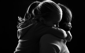 Black and white image of a little girl hugging her mother