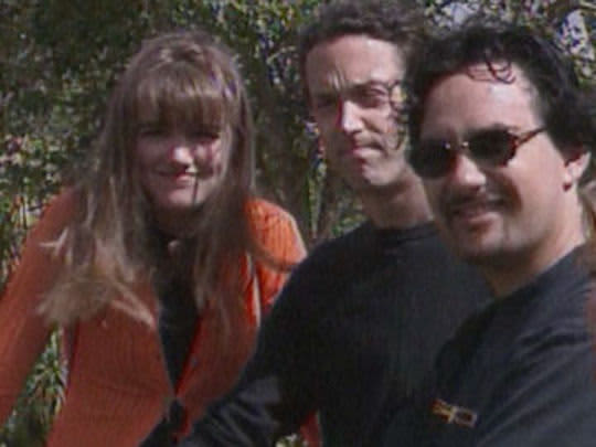 A young woman and two young men stand in the sun, squinting at the camera.