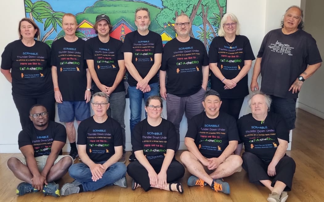 The New Zealand Scrabble team pose for a photo in two rows, all smiling at the camera and wearing team shirts.