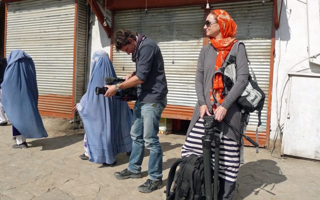 Pietra Brettkelly (right) standing outside in Afghanistan, where she is filming. A man stands next to her holding a camera. There are also two women wearing blue burqa.