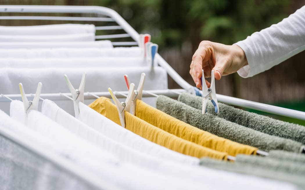 cropped shot of female hand hang fresh terry towels and fabric apparel on metal drying rack and using plastic clothespin in yard after laundry, housework duties