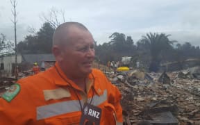 Principal rural fire officer Paul Shaw with the charred remains of one of the houses destroyed by the fire.