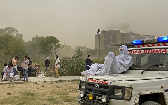 A driver wearing protective gear sits on the bonnet of an ambulance while waiting for the dead body of a Covid-19 coronavirus victim to be taken for burial at a graveyard in New Delhi on April 16, 2021.