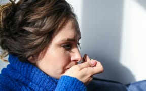 A woman in a blue jumper takes a pill and holds a mug.