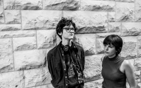 Liam Hansen and Frances Wright, co-hosts of Auckland student radio arts show Various Artists, stand in front of a concrete block wall.