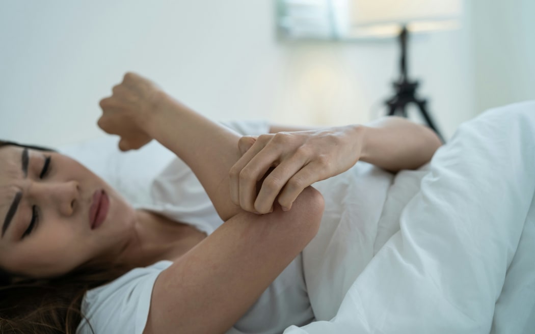 A woman lying in bed and itching her arm.