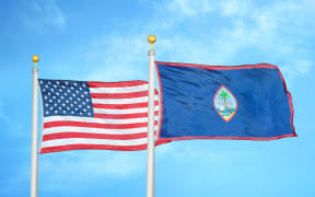United States and Guam two flags on flagpoles and blue cloudy sky background