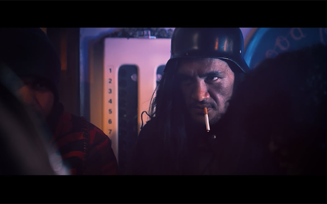 Long-haired Māori man wearing an army helmet with a cigarette hanging out of his mouth
