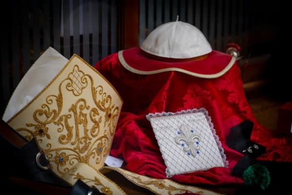 The garments traditionally worn by new popes, including an embroidered mitre, red mozzetta, and a skull cap.
