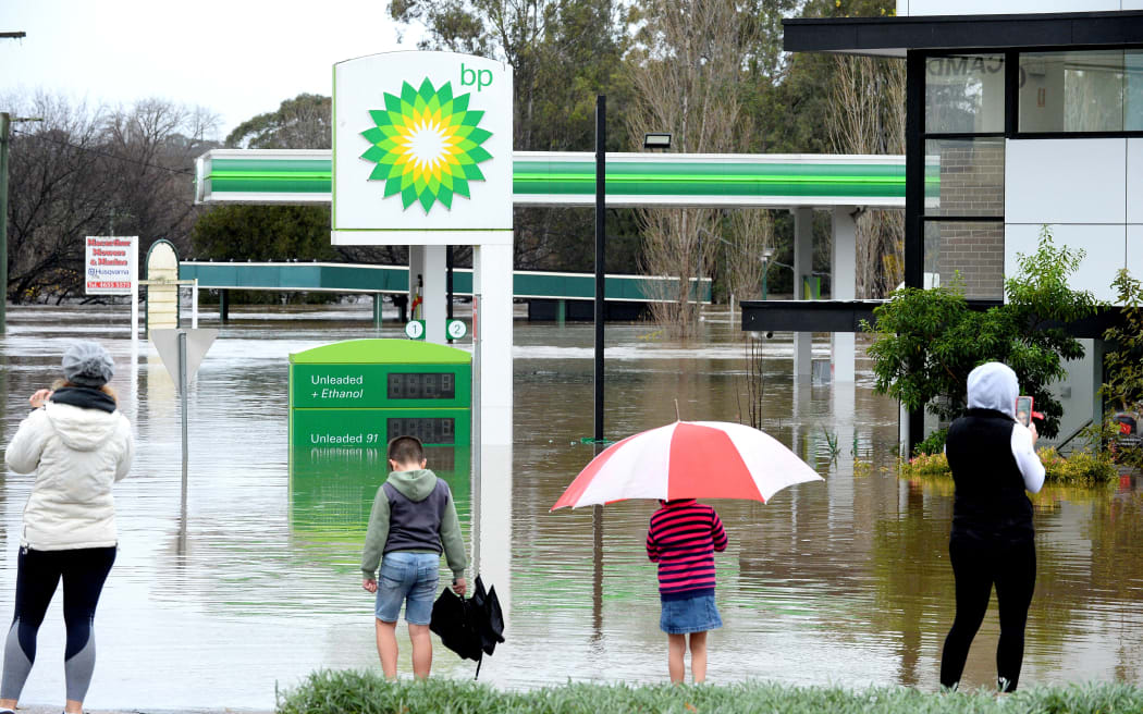 People stand next to a flooded petrol station due to torrential rain in the Camden suburb of Sydney on July 3, 2022. - Thousands of Australians were ordered to evacuate their homes in Sydney on July 3 as torrential rain battered the country's largest city and floodwaters inundated its outskirts. (Photo by Muhammad FAROOQ / AFP)