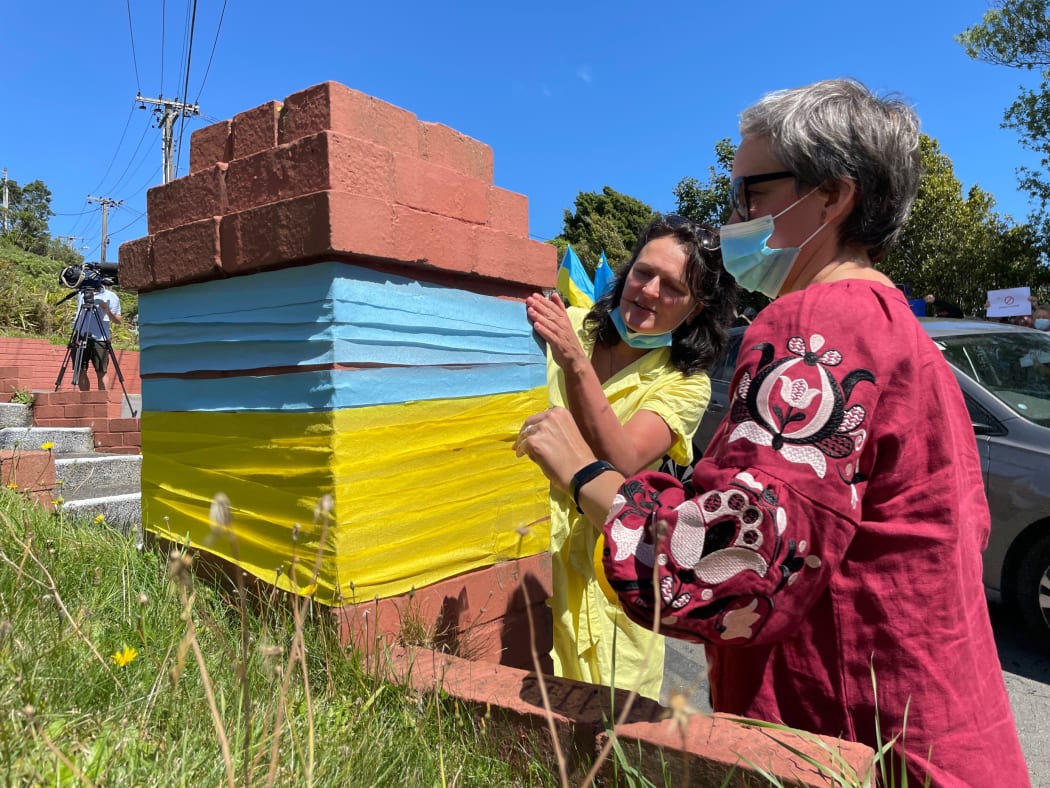 Tetiana Zhurba  (left) and Nataliya Stepuroi put the colours of the Ukranian flag around a brick post by the embassy's driveway.