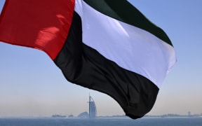 Emirati flag fluttering above Dubai's marina with the Burj Al Arab landmark hotel (C) in the background.