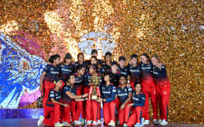Royal Challengers Bangalore's players (including Sophie Devine) hold the trophy after winning the 2024 Women's Premier League (WPL) Twenty20 cricket final match against Delhi Capitals.