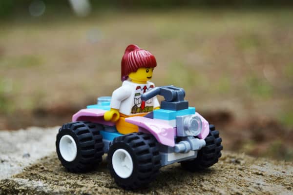 A female Lego figure drives a toy car.