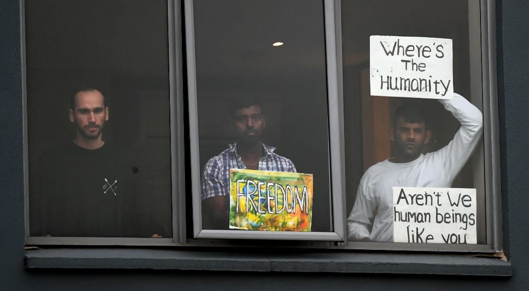 Three asylum seekers gesture to protesters holding a pro-refugee rights rally from their hotel room where they have been detained in Melbourne on June 13, 2020, after they were evacuated to Australia for medical reasons from offshore detention centres on Nauru and Manus Island.