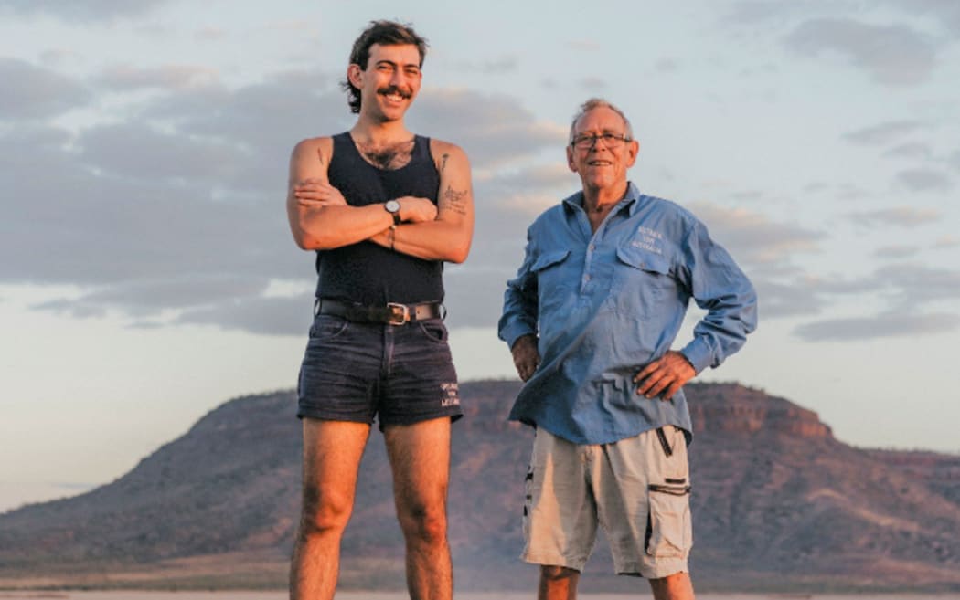 Man in his 20s wearing a singlet and short shorts with his grandad in the Australian outback.