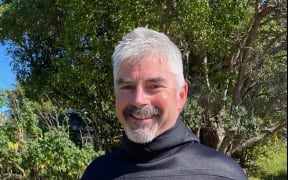 Craig smiles at the camera. He is wearing a wetsuit.