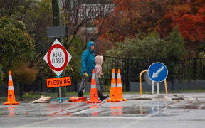A woman and her child walk past a road closure due to flooding sign boardÂ in Christchurch, NewÂ Zealand on May 30, 2021.