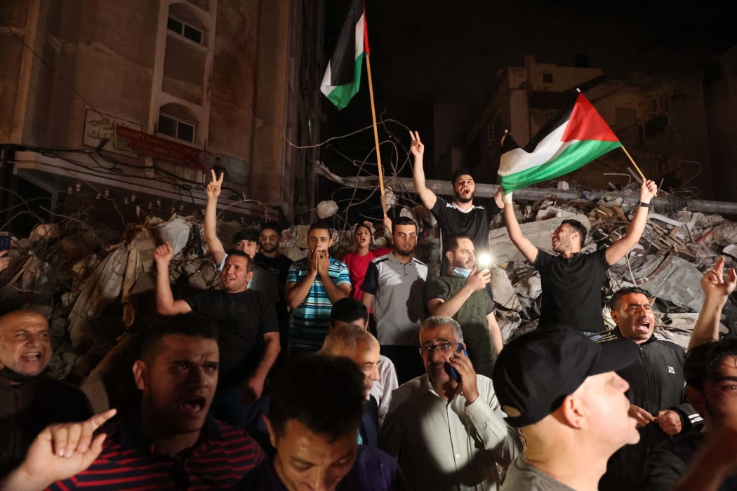 A man waves the Palestinian flag as others flash the V-sign for victory as they celebrates in front of a destroyed building the ceasefire brokered by Egypt between Israel and the two main Palestinian armed groups in Gaza on 20 May 2021.