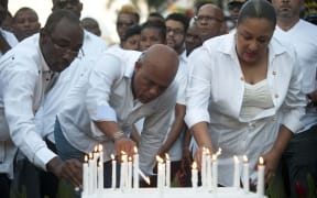 Haitian President Michel Martelly (C) places a candle with First Lady Sophia Martelly (R), and Prime Minister of Haiti, Evans Paul (L), at the site of an accident during the march convened by the government in Port-au-Prince on February 17, 2015