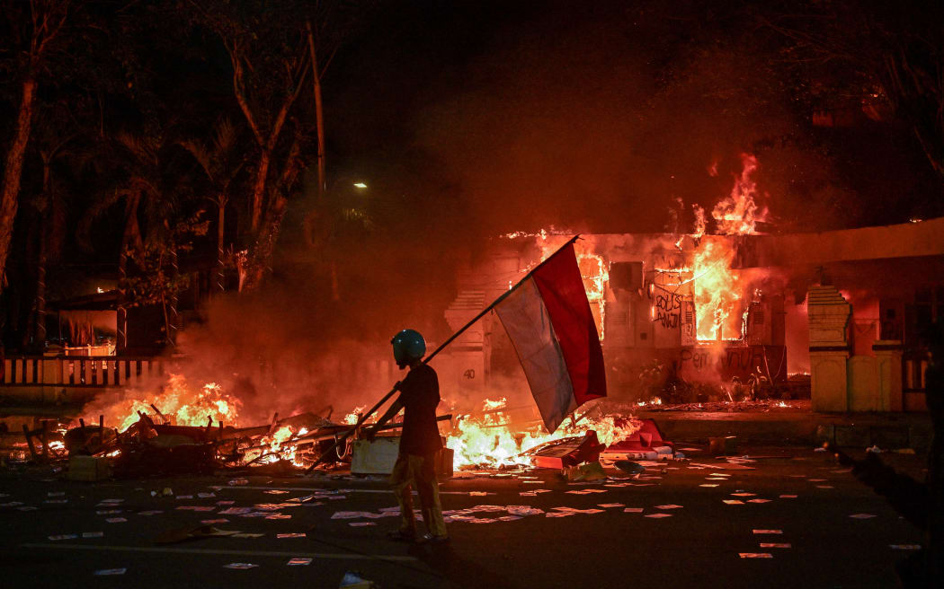 A protester walks with an Indonesian flag in front of a police headquarters that was set on fire and looted.