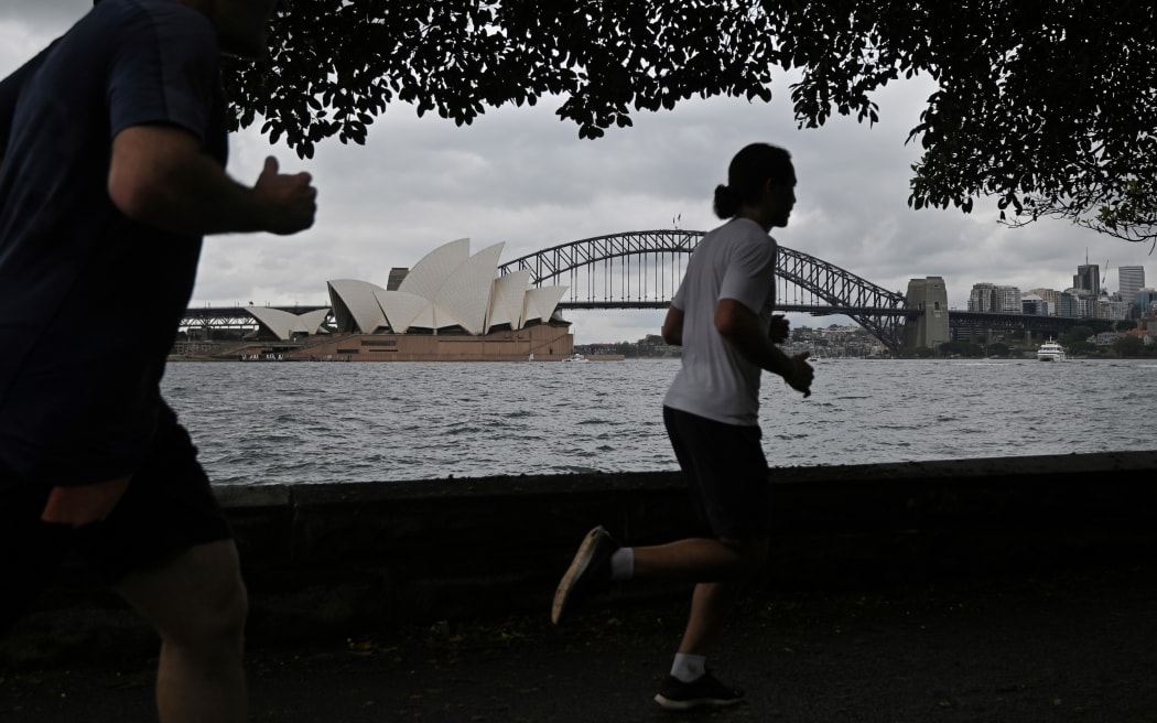 People run before the Opera House and Harbour Bridge in Sydney on December 20, 2020, after authorities introduced a fresh round of restrictions.