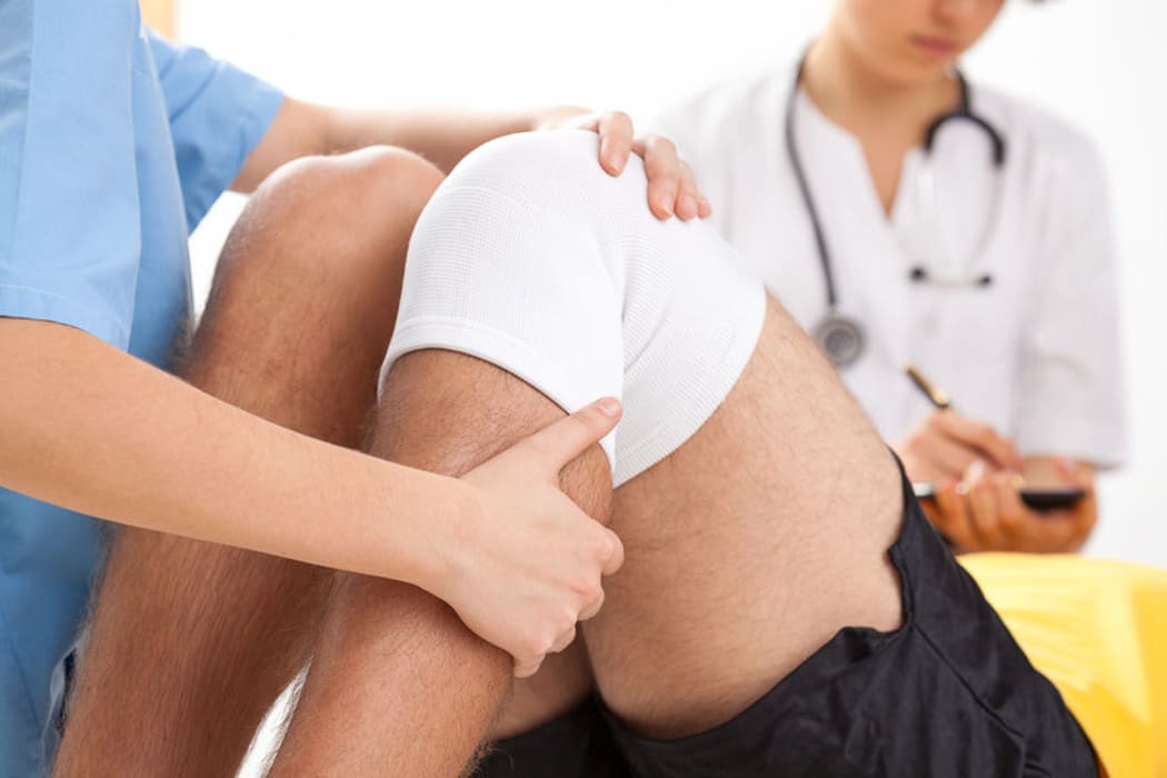 A doctor supervises the recovery of a patient's knee surgery.