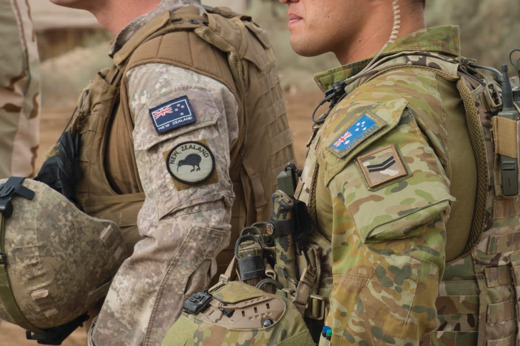 Close up of New Zealand and Australian soldiers side by side in uniform with their country flag on their sleeves.