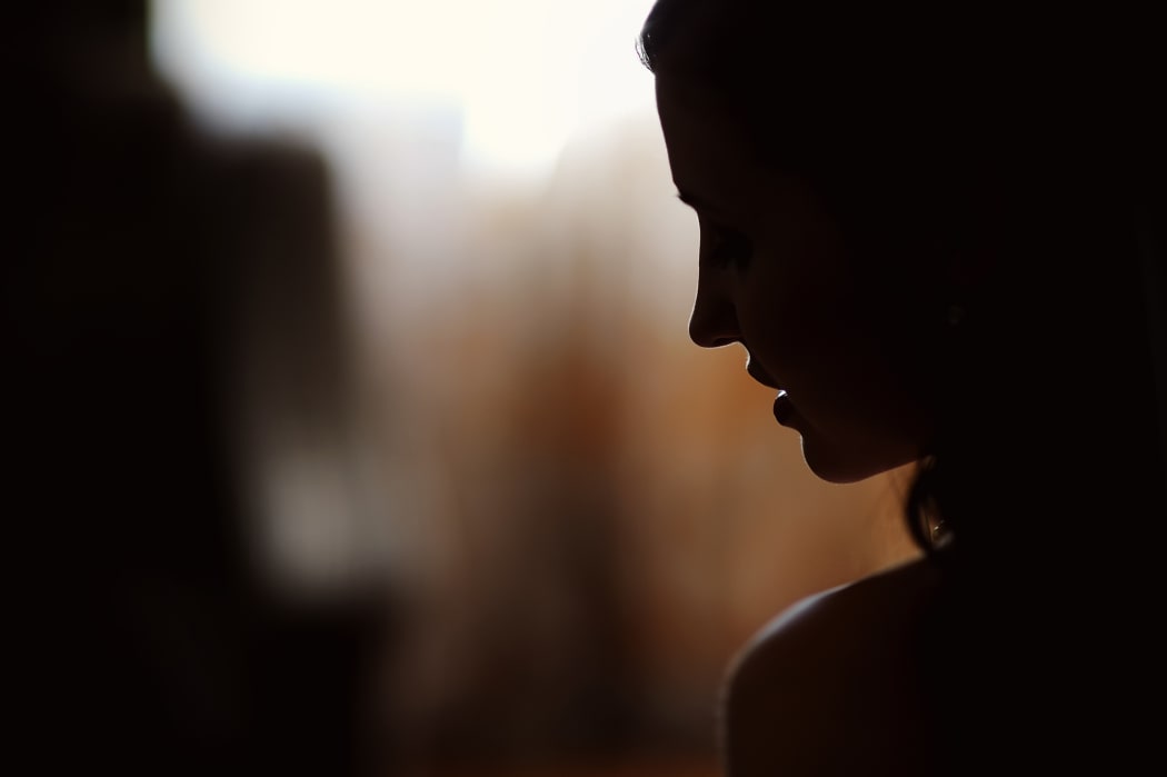 A young woman stands in silhouette against a window.