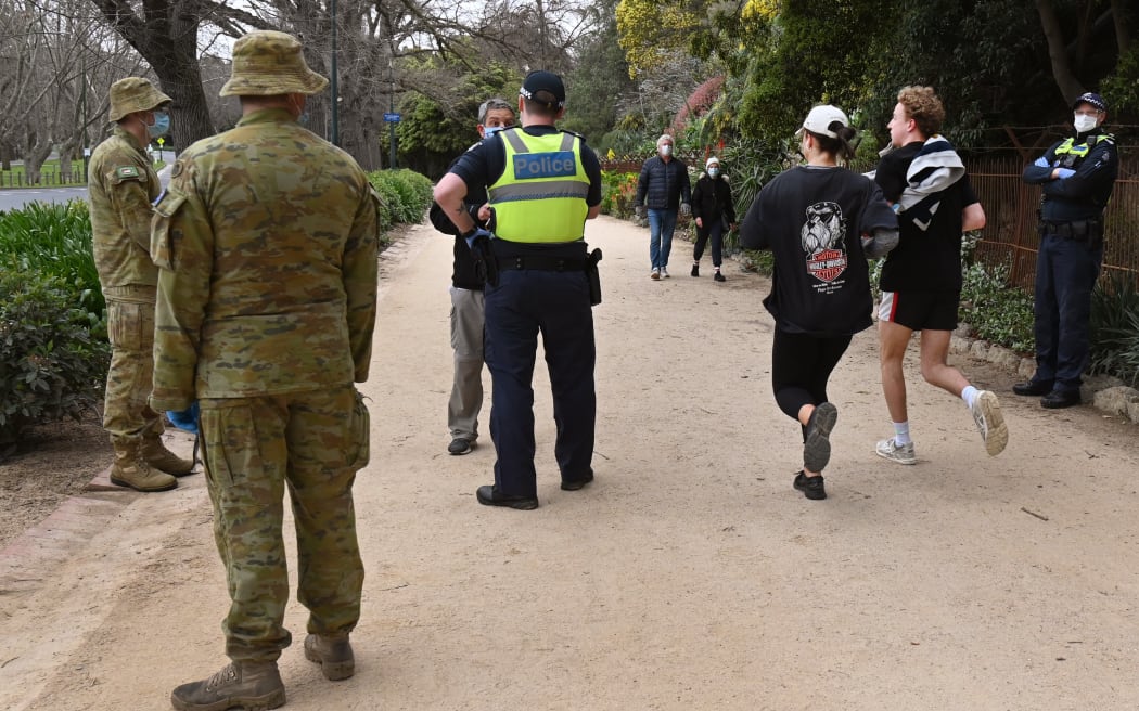 Police and soldiers patrol a running track while people exercise in Melbourne on 7 August 2020, as the city goes into a strict new lockdown after an outbreak of the Covid-19 coronavirus.
