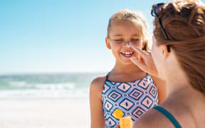 A mother applies protective sunscreen to her daughter's nose at beach.
