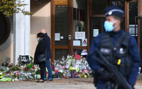 People look at flowers layed outside the Bois d'Aulne secondary school in homage to slain history teacher Samuel Paty.