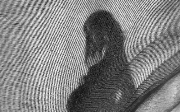 Silhouette of stylish pregnant woman in stylish black dress holding belly bump and posing in light. Stylish fashionable mom, hugging belly, waiting for baby. Creative photo through textile