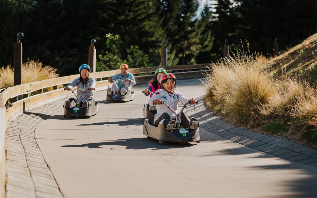 International tourists enjoy riding luge carts at Skyline Queenstown, experiencing thrilling downhill tracks with stunning views.