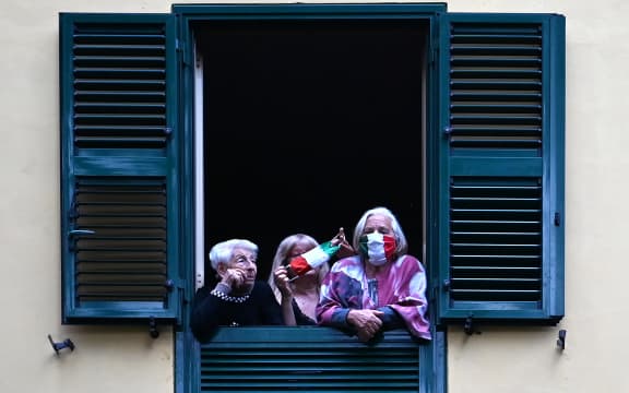 People with protective masks look from their windows at artists performing for the show Sotto lo Stesso Cielo tour (Under the Same Sky tour) in Rome on 18 April 2020.