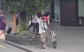 A man uses bolt cutters to snip through a bicycle lock while surrounded by shoppers in Newmarket, Auckland
