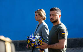 This handout photo taken and released by the Ukrainian presidential press service on 24 August, 2022, shows Ukrainian President Volodymyr Zelensky and wife Olena attending a commemoration ceremony at a memorial wall displaying images of Ukrainian servicemen and servicewomen killed since Russia launched a military invasion on the country in February, in the centre of Kyiv, on Ukraine's Independence Day.