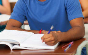 A young man in a classroom, writing, in a file photo to illustrate foreign students.