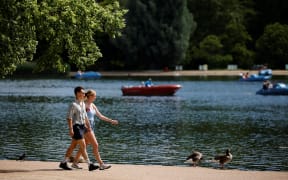People walk in the sunshine in past the boating lake in Hyde Park in London on 14 June 2021.