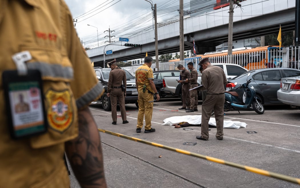 Thai police stand next to a covered body as they inspect the scene after four security guards were killed in a shooting at Or Tor Kor Market in Bangkok on July 28, 2025. A gunman killed four security guards and wounded one other person in a mass shooting at a popular fresh food market in Thailand's capital on July 28, police said. (Photo by Chanakarn Laosarakham / AFP)