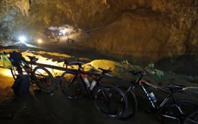 Bicycles belonging to members of a children's football team, who are trapped in a cave chamber along with their coach, are seen as Thai rescue personnel (background) conduct operations under floodlights at the entrance to Tham Luang cave at the Khun Nam Nang Non Forest Park in Chiang Rai.