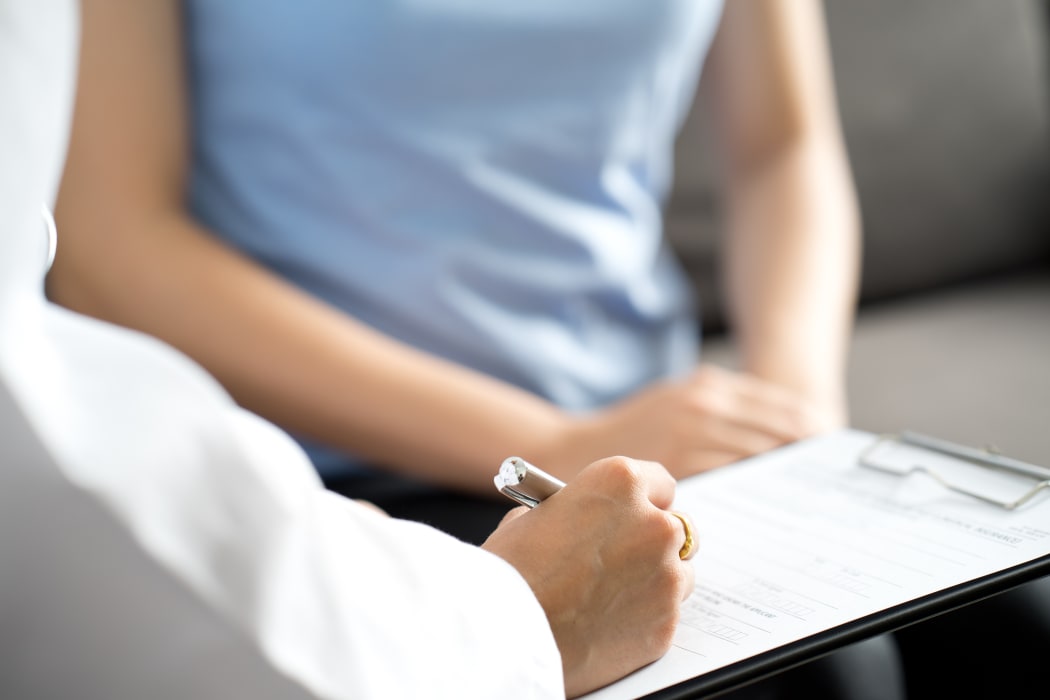A medical professional takes notes while talking to a female patient.