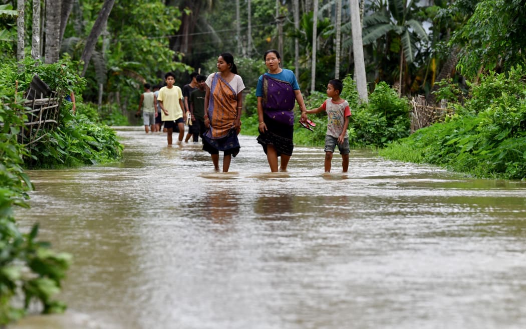 Villagers wade through a flooded street after heavy rains in Kampur at Nagaon district, in India's northeastern state of Assam on June 1, 2025. Flash floods and landslides after torrential monsoon rain over the last two days killed at least 30 people in India's northeast, officials said on June 1. (Photo by Biju BORO / AFP)