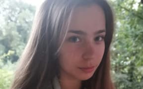 A selfie of Elizabeth who has long brown hair and a slight smile on her face. There are trees behind her and it looks like she is on a deck.