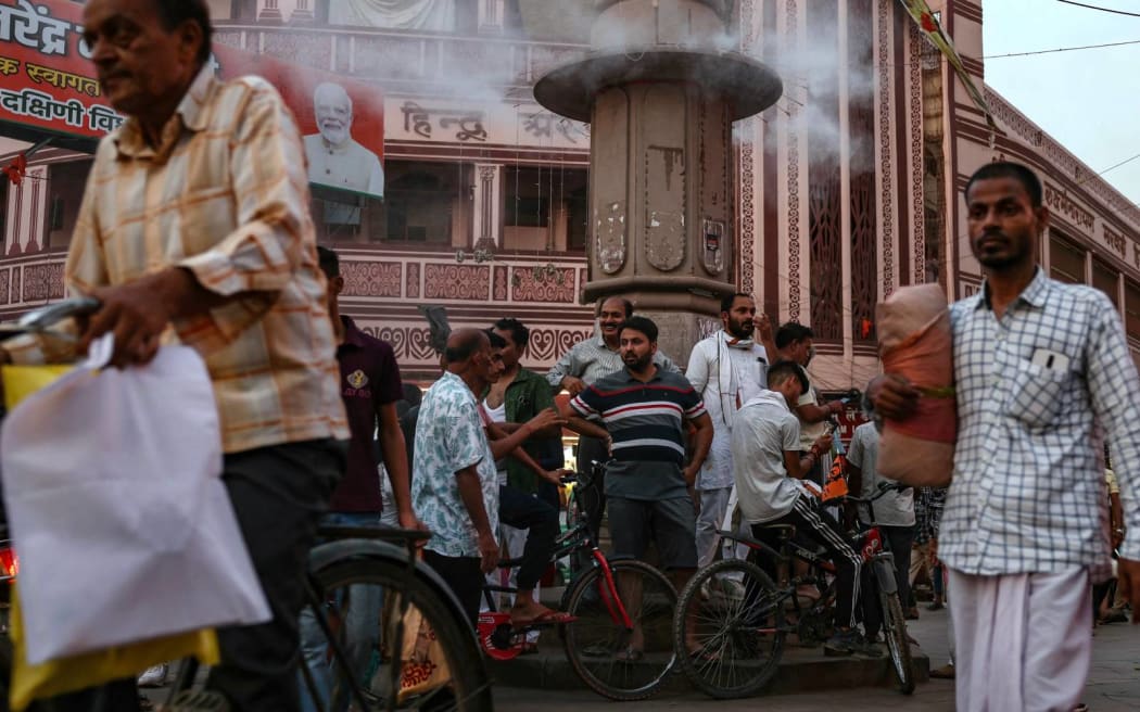 People stand below a water sprinkler installed on a pillar, to cool off, at a market place, amid heatwave in Varanasi on May 31, 2024. (Photo by Niharika KULKARNI / AFP)